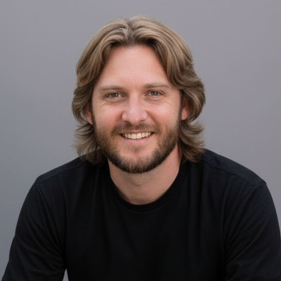 Man with long hair and beard wearing a black t-shirt and gray shorts sitting on a gray background
