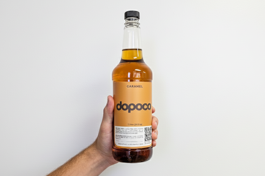 Hand holding a bottle of Dopaco caramel syrup against a white background