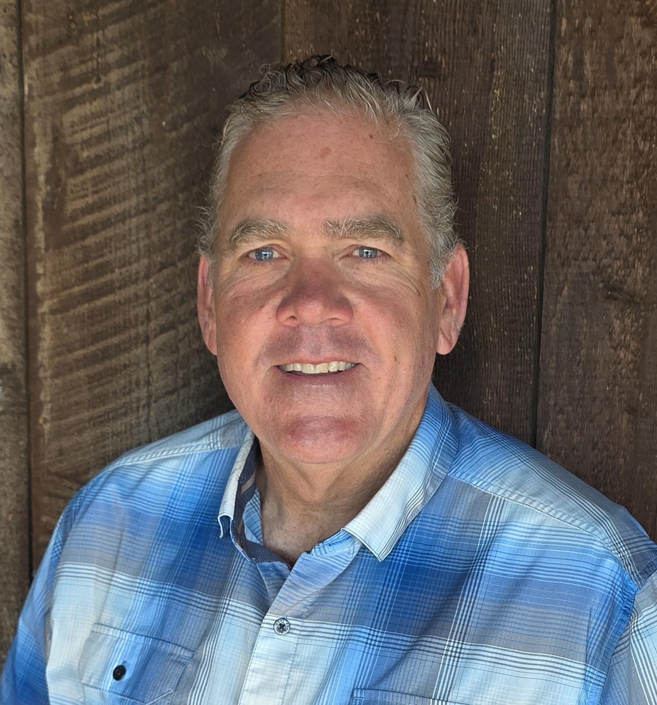 Man wearing a blue plaid shirt against a wooden background